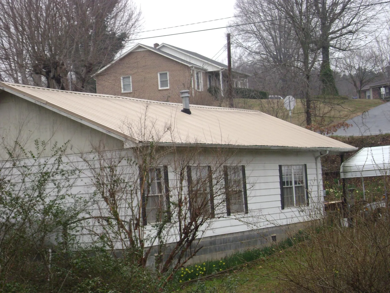 Tan metal roof on a white sided house set into a hillside — Commercial Roofing by Roofing Brothers in O Fallon